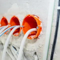 Pomarańczowe puszki instalacyjne z przewodami, gotowe do montażu gniazdek. To początek samodzielnej instalacji elektrycznej.