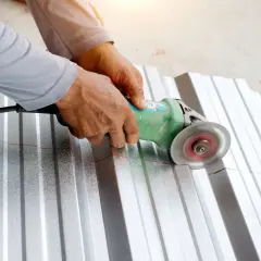 Ręce trzymają szlifierkę kątową, która tnie falistą blachę aluminiową. To pokazuje, czym ciąć aluminium.