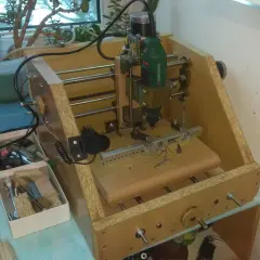 Domowa budowa frezarki CNC z narzędziami i rośliną w tle.