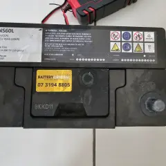 Akumulator DEL-NS60L, podłączony do ładowarki, lekko bulgocze podczas ładowania.