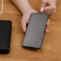 Ręka podłącza kabel do telefonu, pokazując, jak ładować baterie litowo jonowe za pomocą powerbanku.
