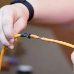 Dłonie trzymają przerwany pomarańczowy kabel, pokazując, jak połączyć przerwany kabel. Izolacja jest nacięta, a przewody widoczne.