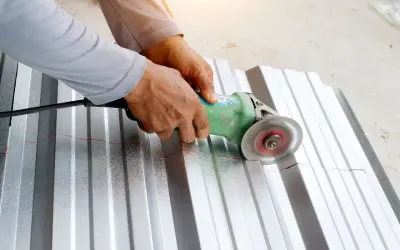 Ręce trzymają szlifierkę kątową, która tnie falistą blachę aluminiową. To pokazuje, czym ciąć aluminium.
