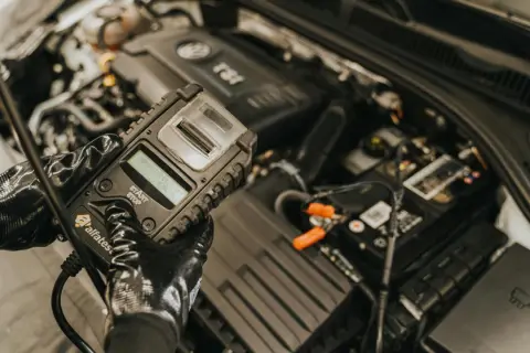 Mechanik w rękawiczkach sprawdza stan akumulatora za pomocą testera. To kluczowy etap diagnostyki, zapobiegający problemom z rozruchem, czyli gazowanie akumulatora.
