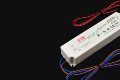 Zasilacz LED z oznaczeniami napięcia i mocy. Urządzenie ma białą obudowę i kable w kolorach czerwonym, czarnym, brązowym i niebieskim.