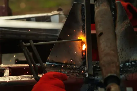 Spawanie elektrodą, iskry lecą, widoczna czerwona rękawica. Widać potencjalne błędy przy spawaniu elektrodą.