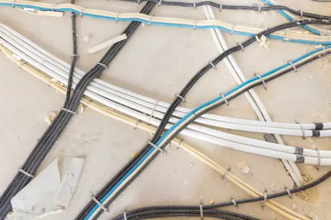 Uporządkowane kable w peszlach na betonowym podłożu. Widać różne kolory peszli: czarny, biały, żółty i niebieski. To przykład, jak przeciągnąć kabel przez peszel.
