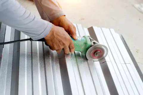 Ręce trzymają szlifierkę kątową, która tnie falistą blachę aluminiową. To pokazuje, czym ciąć aluminium.