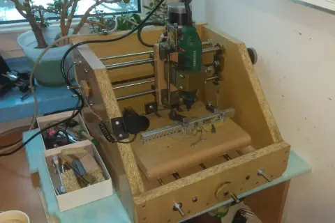 Domowa budowa frezarki CNC z narzędziami i rośliną w tle.