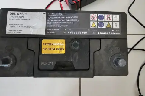 Akumulator DEL-NS60L, podłączony do ładowarki, lekko bulgocze podczas ładowania.