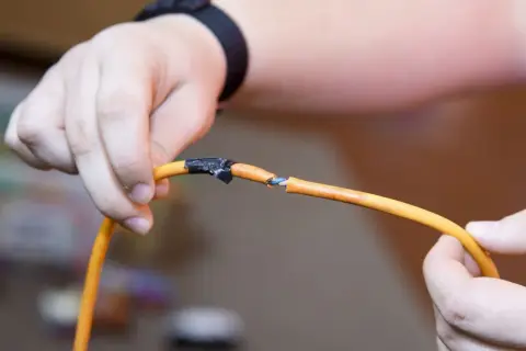 Dłonie trzymają przerwany pomarańczowy kabel, pokazując, jak połączyć przerwany kabel. Izolacja jest nacięta, a przewody widoczne.