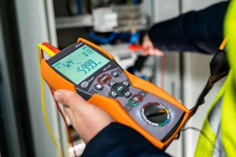 Elektryk wykonuje pomiary elektryczne krok po kroku za pomocą miernika.