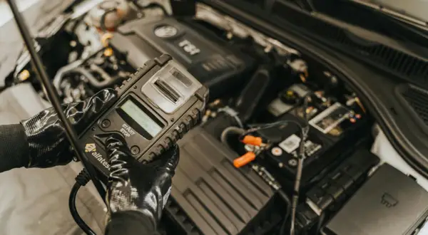 Mechanik w rękawiczkach sprawdza stan akumulatora za pomocą testera. To kluczowy etap diagnostyki, zapobiegający problemom z rozruchem, czyli gazowanie akumulatora.