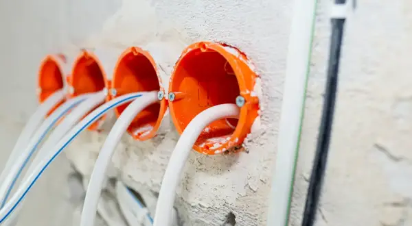 Pomarańczowe puszki instalacyjne z przewodami, gotowe do montażu gniazdek. To początek samodzielnej instalacji elektrycznej.