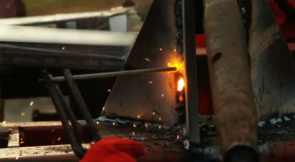 Spawanie elektrodą, iskry lecą, widoczna czerwona rękawica. Widać potencjalne błędy przy spawaniu elektrodą.