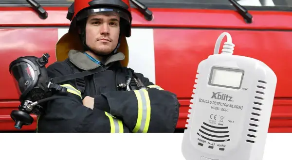 Strażak w hełmie i masce obok czujnika gazu Xblitz. Urządzenie może włączyć alarm bez powodu, sygnalizując potencjalne zagrożenie.