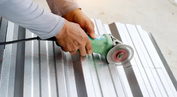 Ręce trzymają szlifierkę kątową, która tnie falistą blachę aluminiową. To pokazuje, czym ciąć aluminium.