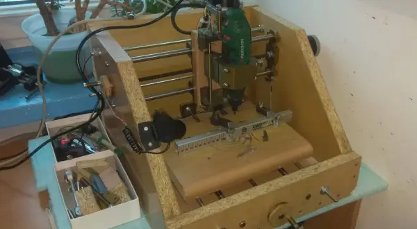 Domowa budowa frezarki CNC z narzędziami i rośliną w tle.