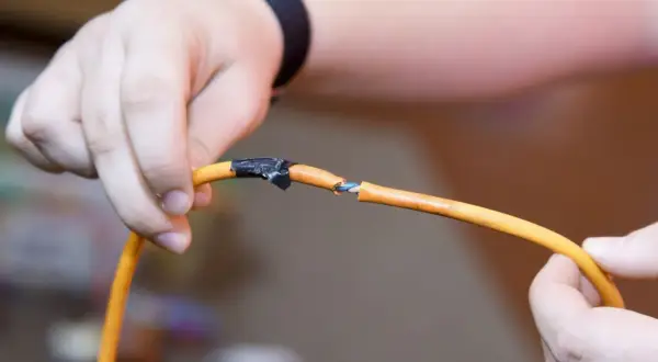 Dłonie trzymają przerwany pomarańczowy kabel, pokazując, jak połączyć przerwany kabel. Izolacja jest nacięta, a przewody widoczne.
