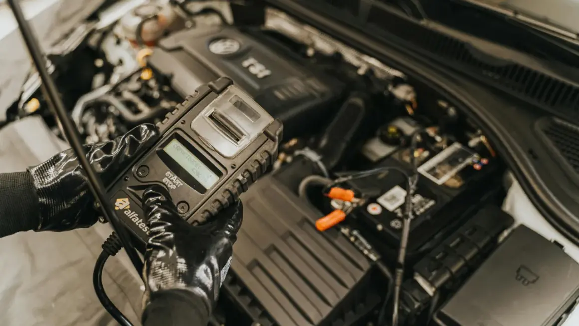Mechanik w rękawiczkach sprawdza stan akumulatora za pomocą testera. To kluczowy etap diagnostyki, zapobiegający problemom z rozruchem, czyli gazowanie akumulatora.