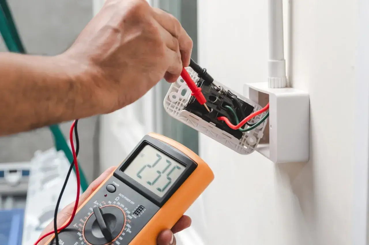 Elektryk sprawdza prąd w obu przewodach gniazdka za pomocą multimetru. Odczyt wskazuje 235V.