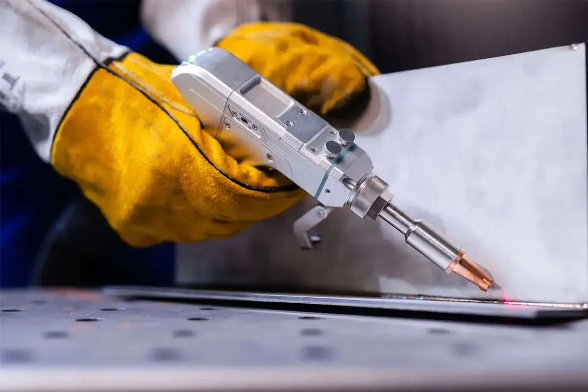 Ręka w żółtej rękawicy trzyma spawarkę laserową, precyzyjnie łącząc metal.