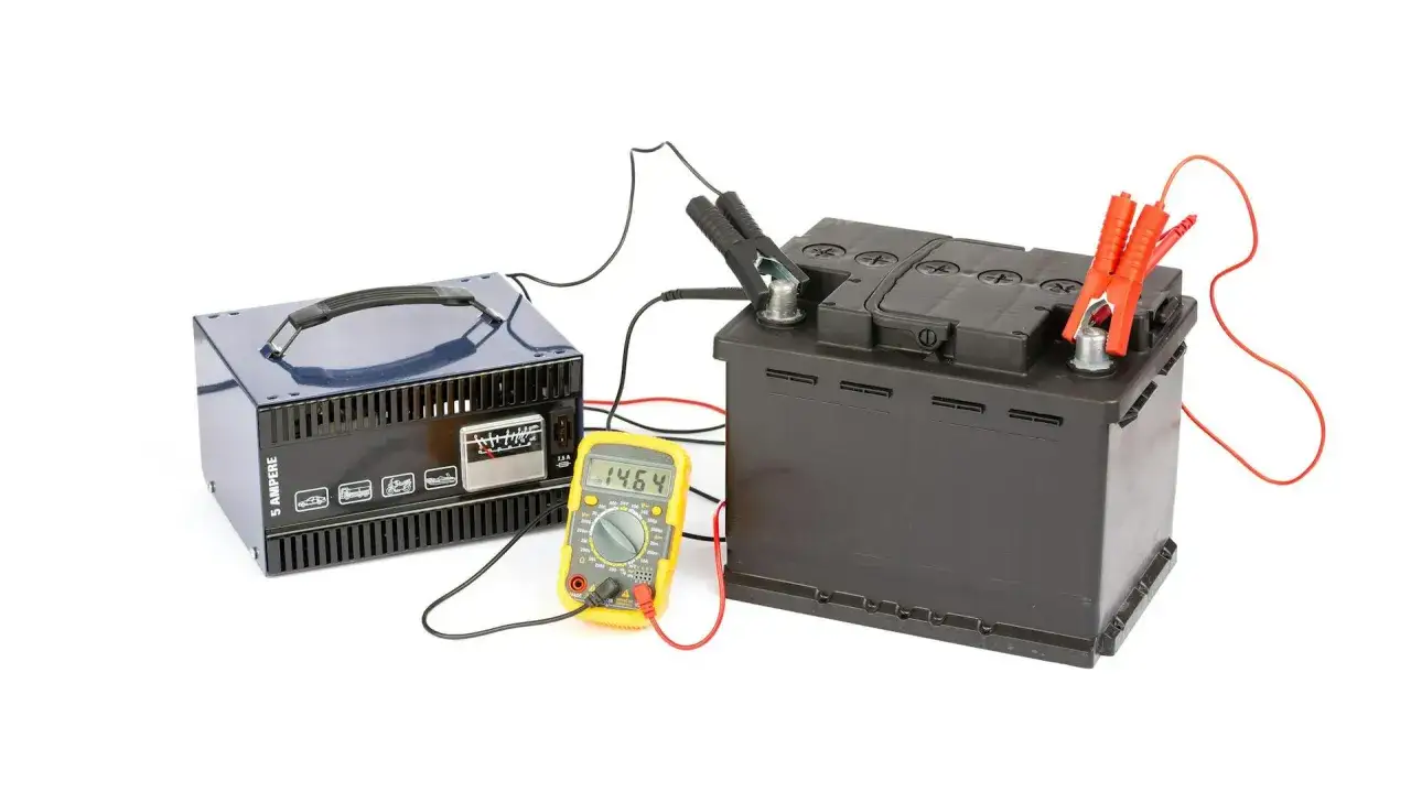 Schemat ładowania akumulatora: prostownik, akumulator i multimetr pokazujący 14.64V.