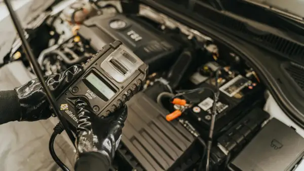 Mechanik w rękawiczkach sprawdza stan akumulatora za pomocą testera. To kluczowy etap diagnostyki, zapobiegający problemom z rozruchem, czyli gazowanie akumulatora.