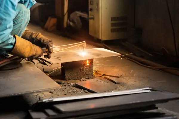 Ręce w rękawicach trzymają palnik, pokazując, jak spawać metal. Iskry lecą podczas pracy.