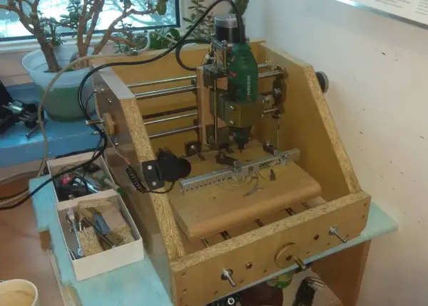 Domowa budowa frezarki CNC z narzędziami i rośliną w tle.