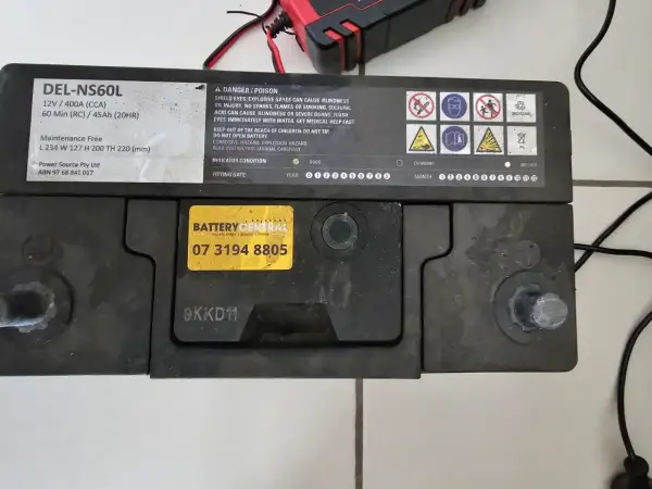 Akumulator DEL-NS60L, podłączony do ładowarki, lekko bulgocze podczas ładowania.